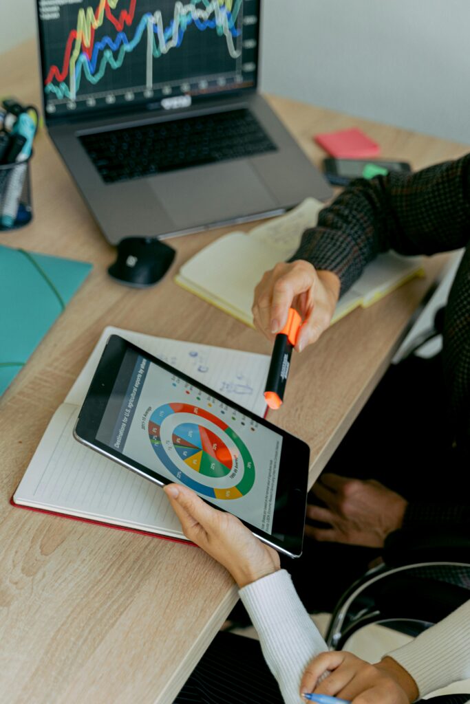 Business professionals analyzing data on tablet during a meeting with laptops and charts.